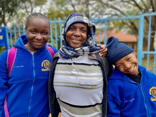 Mom standing between her two kids in their blue school uinforms