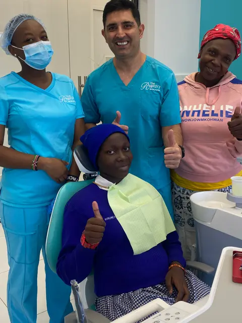 Seated African Girl smiling with doctor and nurse standing behind her.