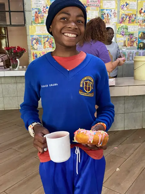 Boy holding mug and food, smiling in blue uniform