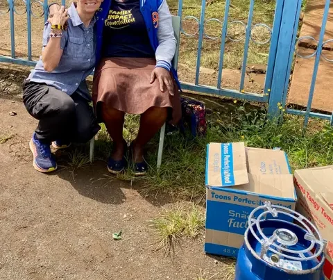 Melody crouched down beside woman in wheel chair in front of blue fence