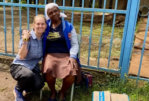 Melody crouched down beside woman in wheel chair in front of blue fence