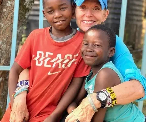 Melody wearing a blue ball cap, with her arms around two East Africna Children.