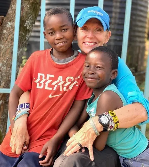 Melody wearing a blue ball cap, with her arms around two East Africna Children.